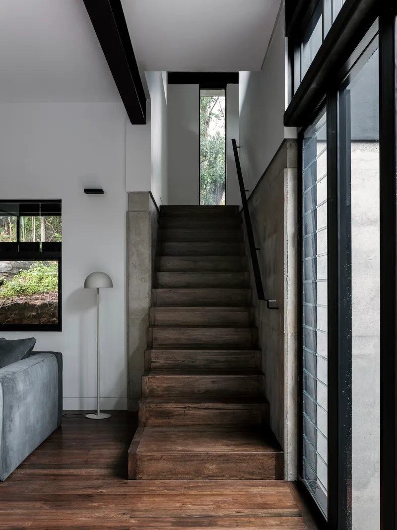 Dark timber staircase with concrete balustrade rising alongside a tall vertical window