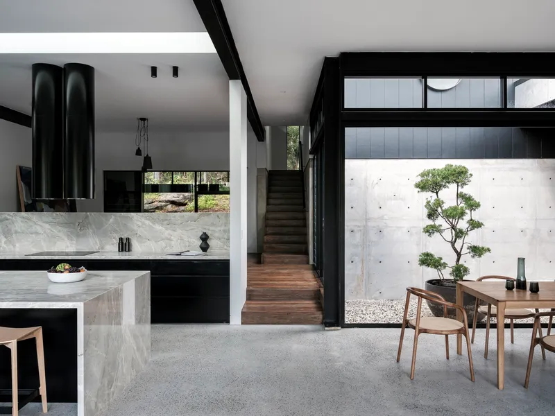 Open-plan kitchen and dining area with marble island, black cabinetry, and courtyard view with bonsai tree