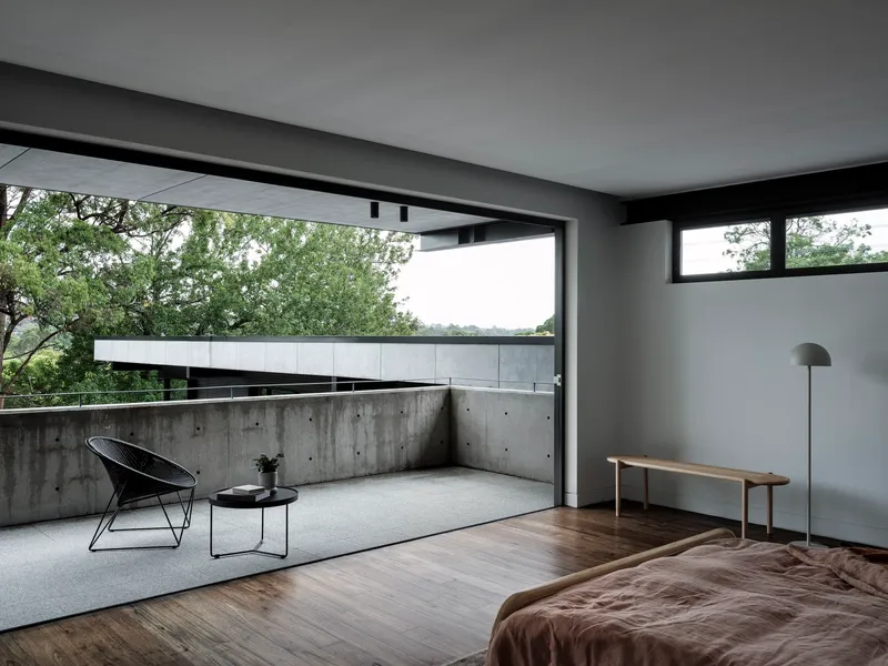 Bedroom opening to concrete terrace with wire chair overlooking leafy canopy