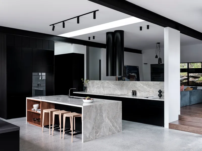 Kitchen with marble island, black joinery, and cylindrical range hood under exposed ceiling beams