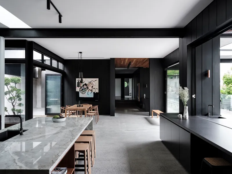 Open-plan kitchen and dining area with black timber walls, marble island, and high clerestory windows