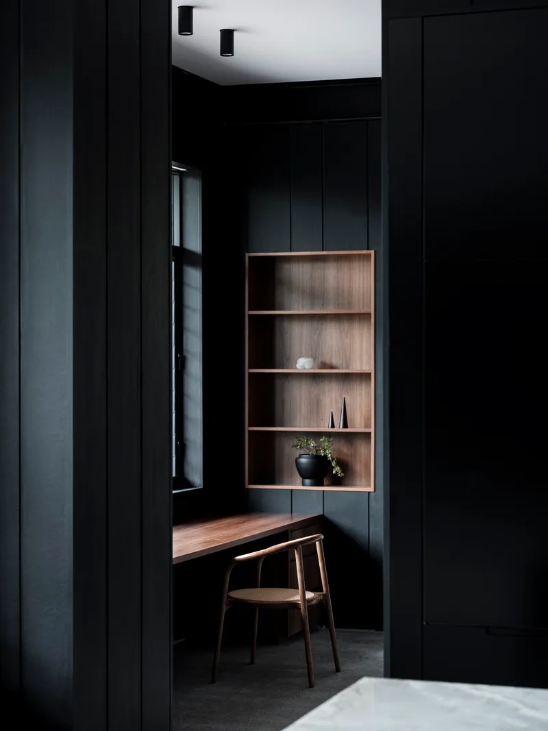 Black paneled study nook with recessed timber shelving and floating desk beneath a white ceiling