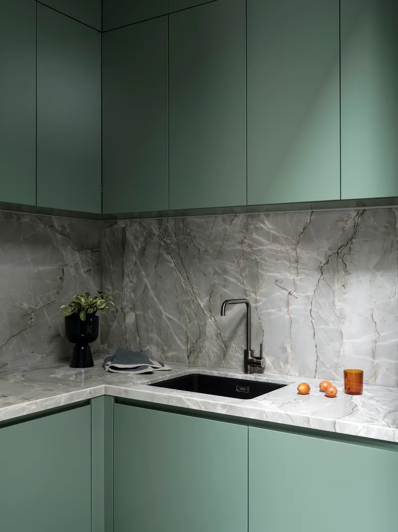Corner kitchen with sage green cabinetry and grey veined marble backsplash and countertop
