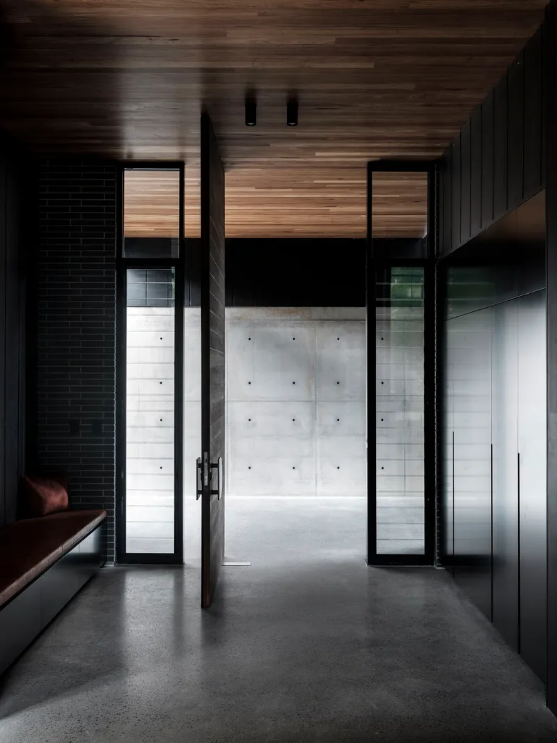 Glass door opening from timber-clad interior hallway to concrete courtyard beyond