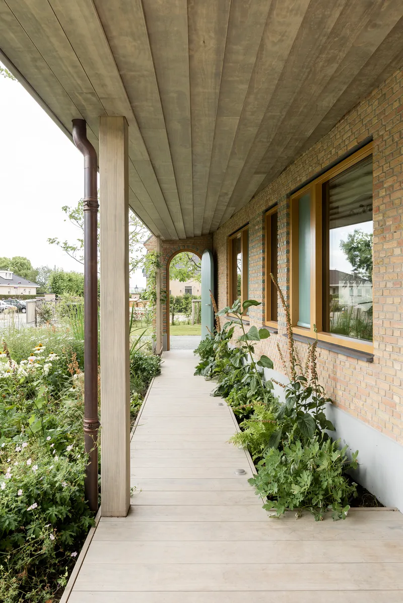 Covered walkway with concrete plank ceiling alongside planted bed and brick wall windows