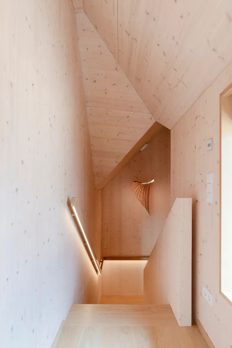 Light-wood-paneled stairwell with a sculptural pendant lamp and daylight from a skylight above