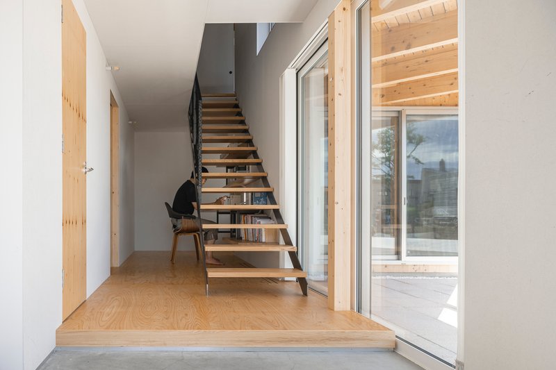 Entry hallway with open timber staircase and plywood flooring leading to glazed doors