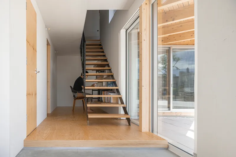Entry hallway with open timber staircase and plywood flooring leading to glazed doors