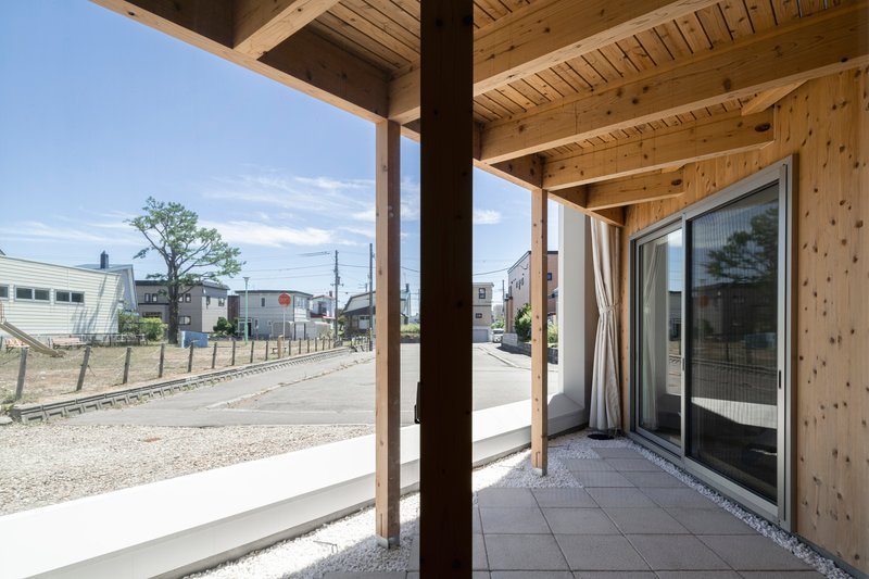 Covered terrace with timber posts and joists overlooking the gravel lot and neighboring houses