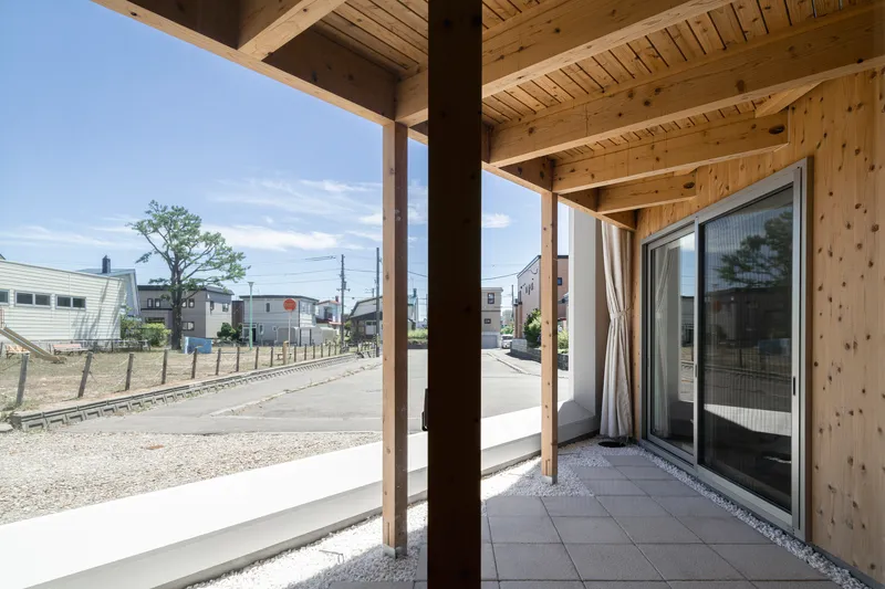 Covered terrace with timber posts and joists overlooking the gravel lot and neighboring houses