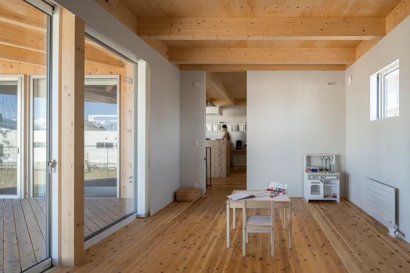 Open living space with exposed timber ceiling beams and a figure moving through the kitchen