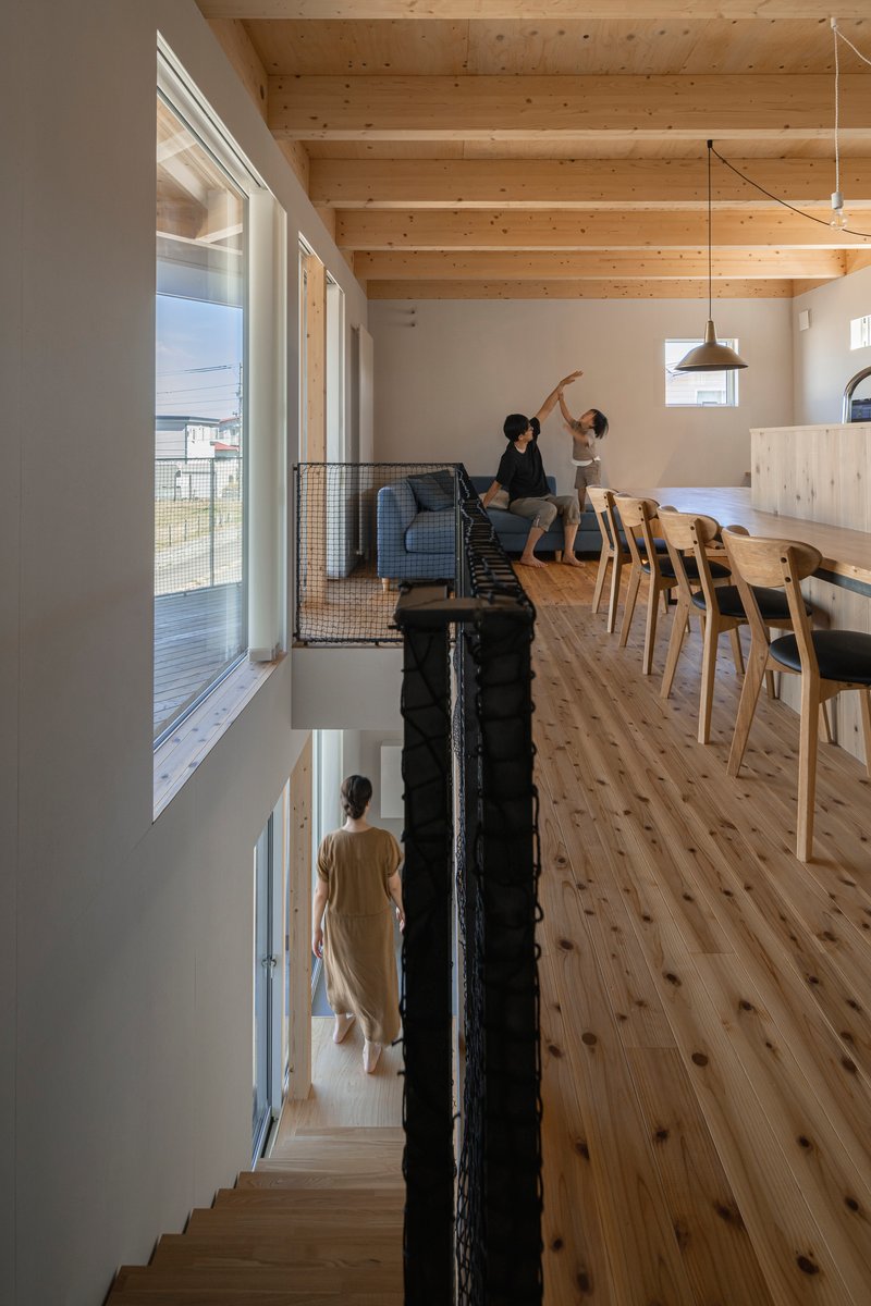 Split-level interior with exposed timber ceiling beams, mesh-rail balustrade, and residents moving through the upper floor