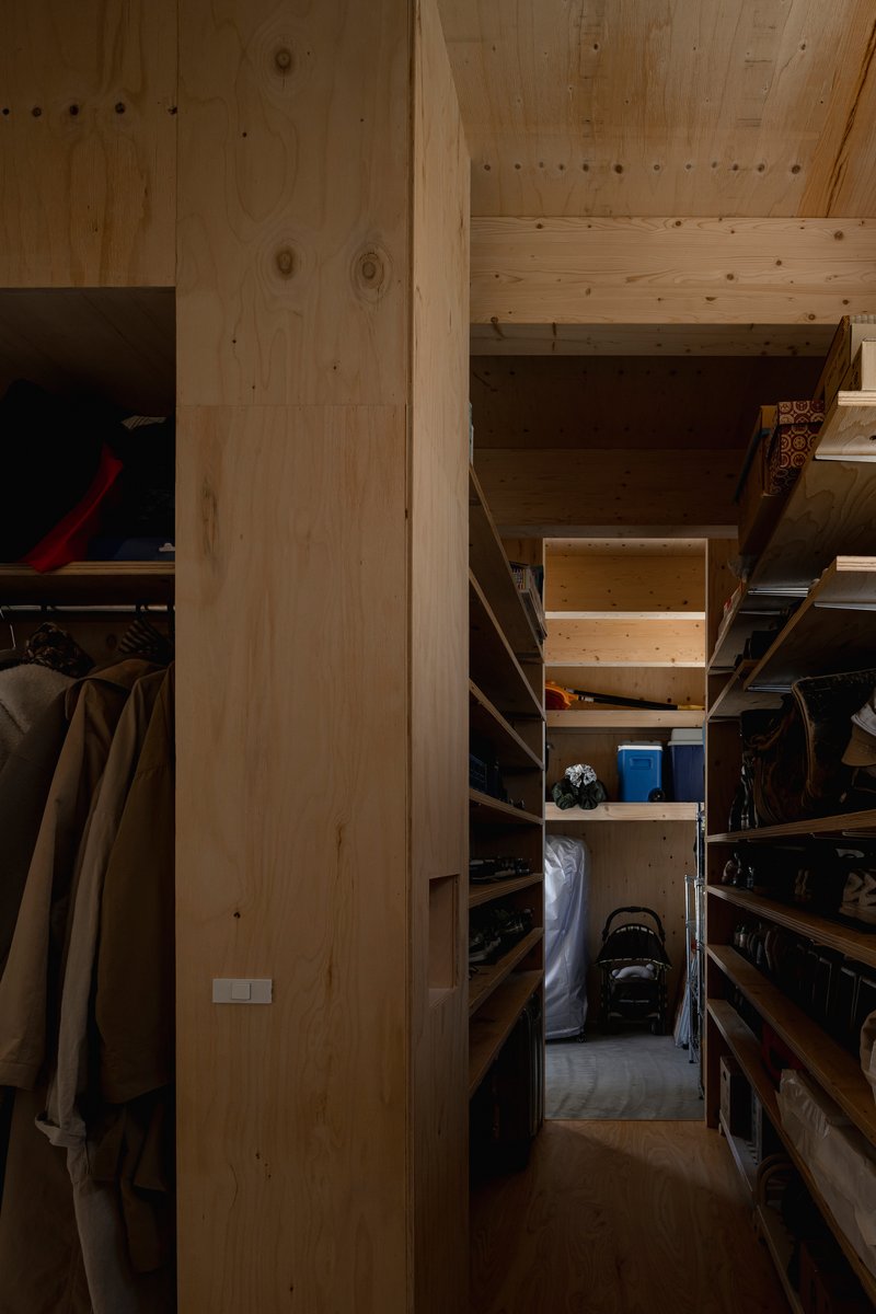 Narrow storage corridor lined with timber shelving under a plywood ceiling in low light