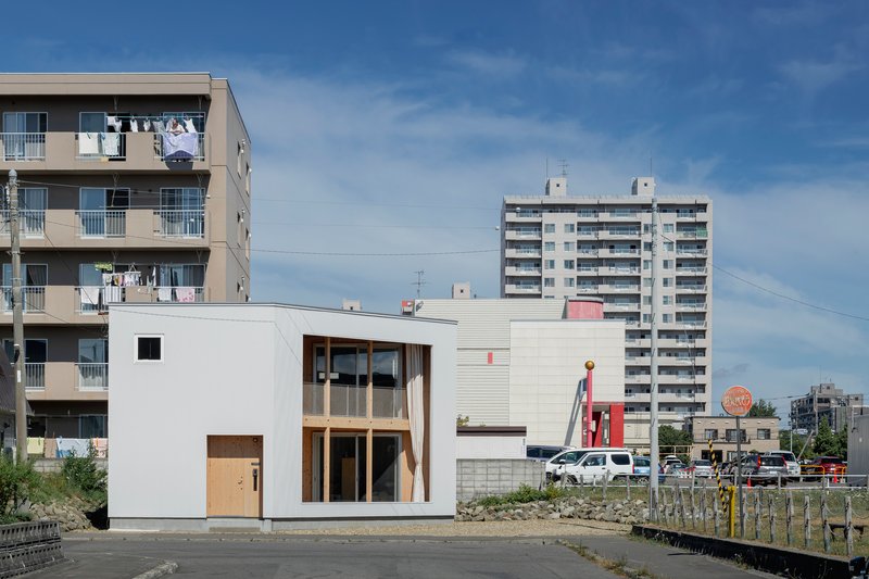 Street view of the white metal-clad volumes against mid-rise apartment buildings under blue sky
