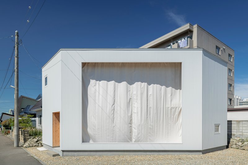 White facade frame with plywood reveals and closed white fabric curtains screening the interior