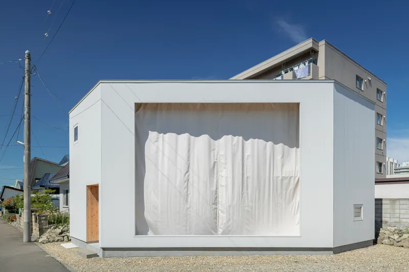 White facade frame with plywood reveals and closed white fabric curtains screening the interior