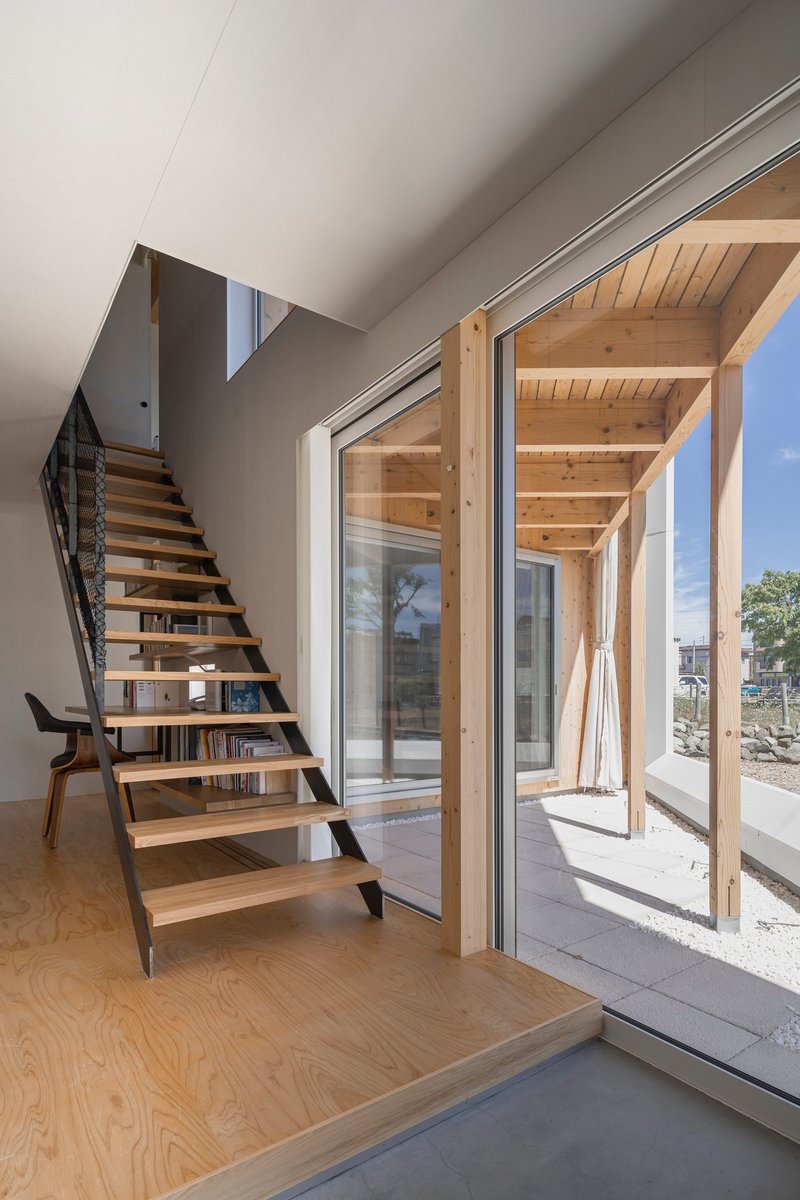 Open-tread timber staircase beside glazed doors leading to the plywood-framed double-height courtyard