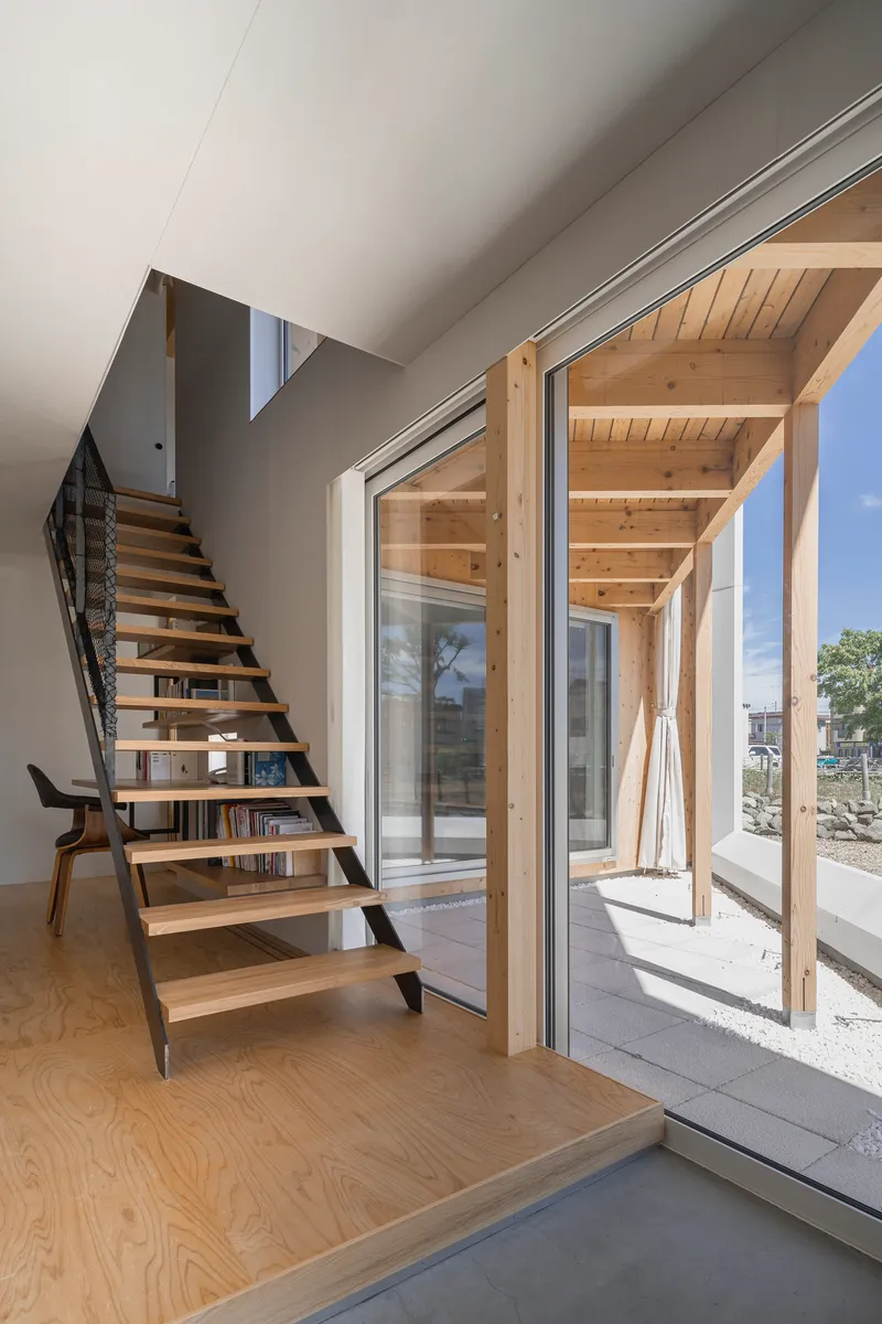 Open-tread timber staircase beside glazed doors leading to the plywood-framed double-height courtyard