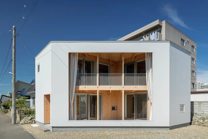 Street view of the white rendered facade with double-height glazed opening and exposed timber framing