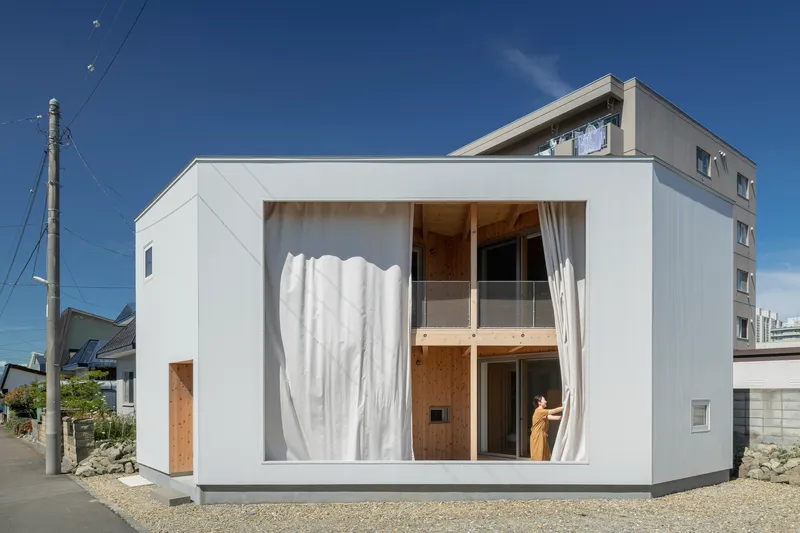 White stucco facade with floor-to-ceiling windows framed by drawn curtains and a figure visible inside