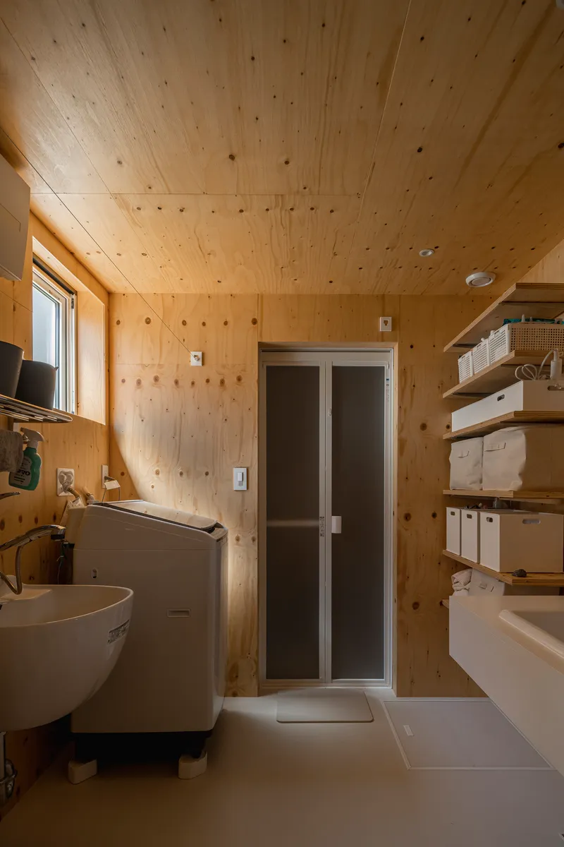 Compact bathroom clad entirely in plywood with wall-mounted sink and frosted glass shower door