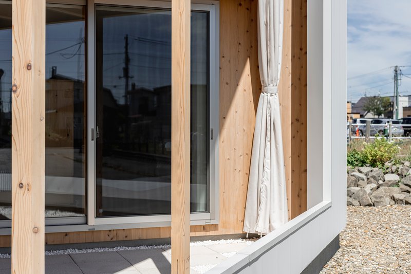 Detail of sliding glass doors framed by exposed timber posts with a tied fabric curtain in bright sunlight