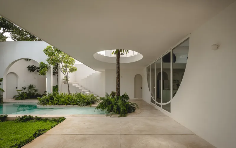 Covered terrace with curved white ceiling and circular skylight overlooking courtyard pool and planted beds