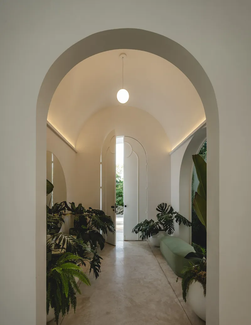 Vaulted corridor with arched openings and pendant light leading to garden beyond