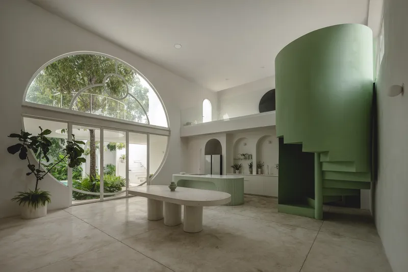 Living space with large circular window, mint green curved staircase, oval table, and courtyard view with potted plants