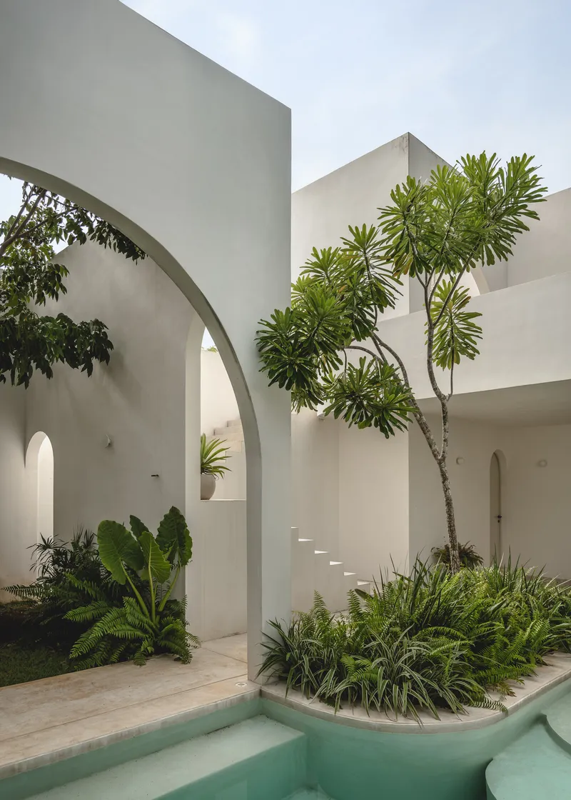 Courtyard with turquoise pool, floating cantilevered stairs, tall palms, and white walls under a cloudy sky