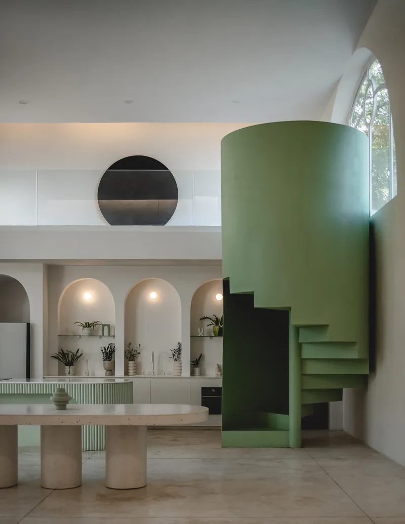 Double-height living space with green cylindrical stair volume and arched kitchen niches lit from within