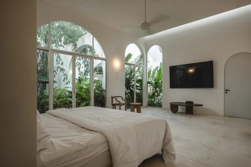 Bedroom with arched windows overlooking a planted courtyard with banana palms in afternoon light