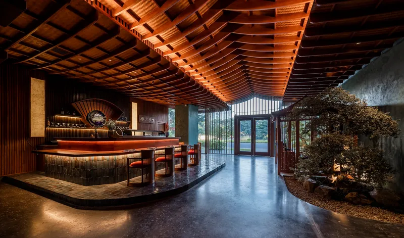 Reception area with curved timber counter and undulating wood-slat ceiling above an interior courtyard with tree