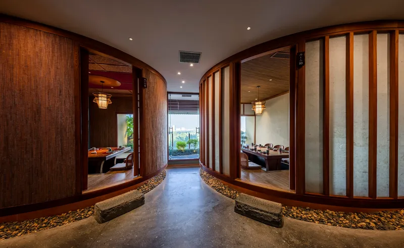 Corridor with curved timber screen walls and river stone flooring flanked by translucent shoji-style partitions