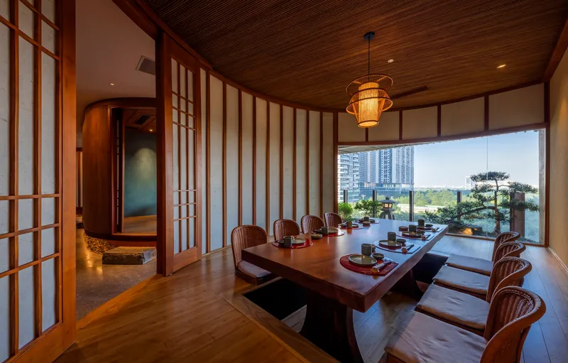 Dining room with low table and sliding shoji screens opening to a terrace with bonsai tree