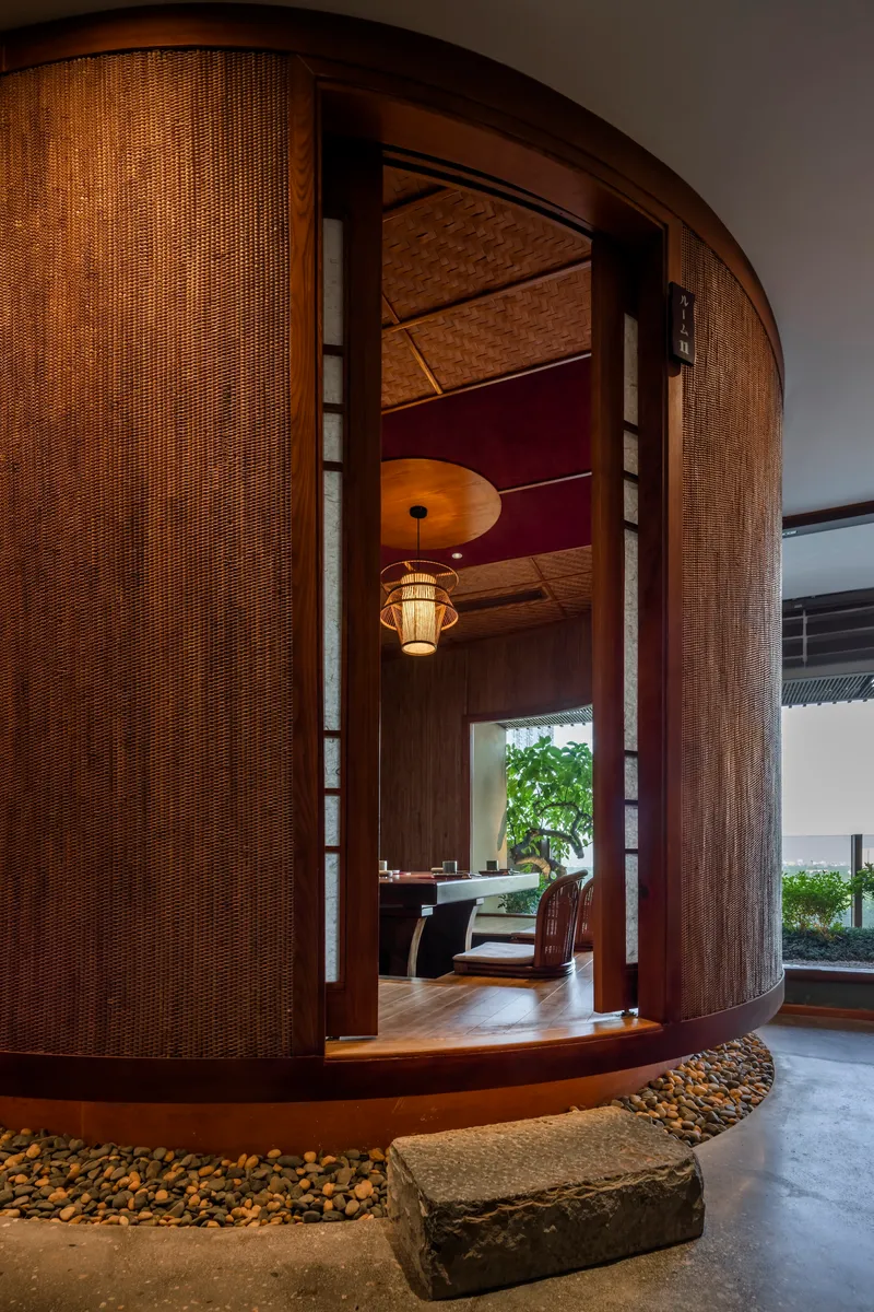 Curved woven rattan entry portal with stone steps surrounded by river pebbles under warm interior lighting
