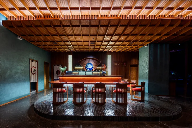 Bar area beneath gridded bamboo ceiling with raised platform, backlit counter and grey plaster walls