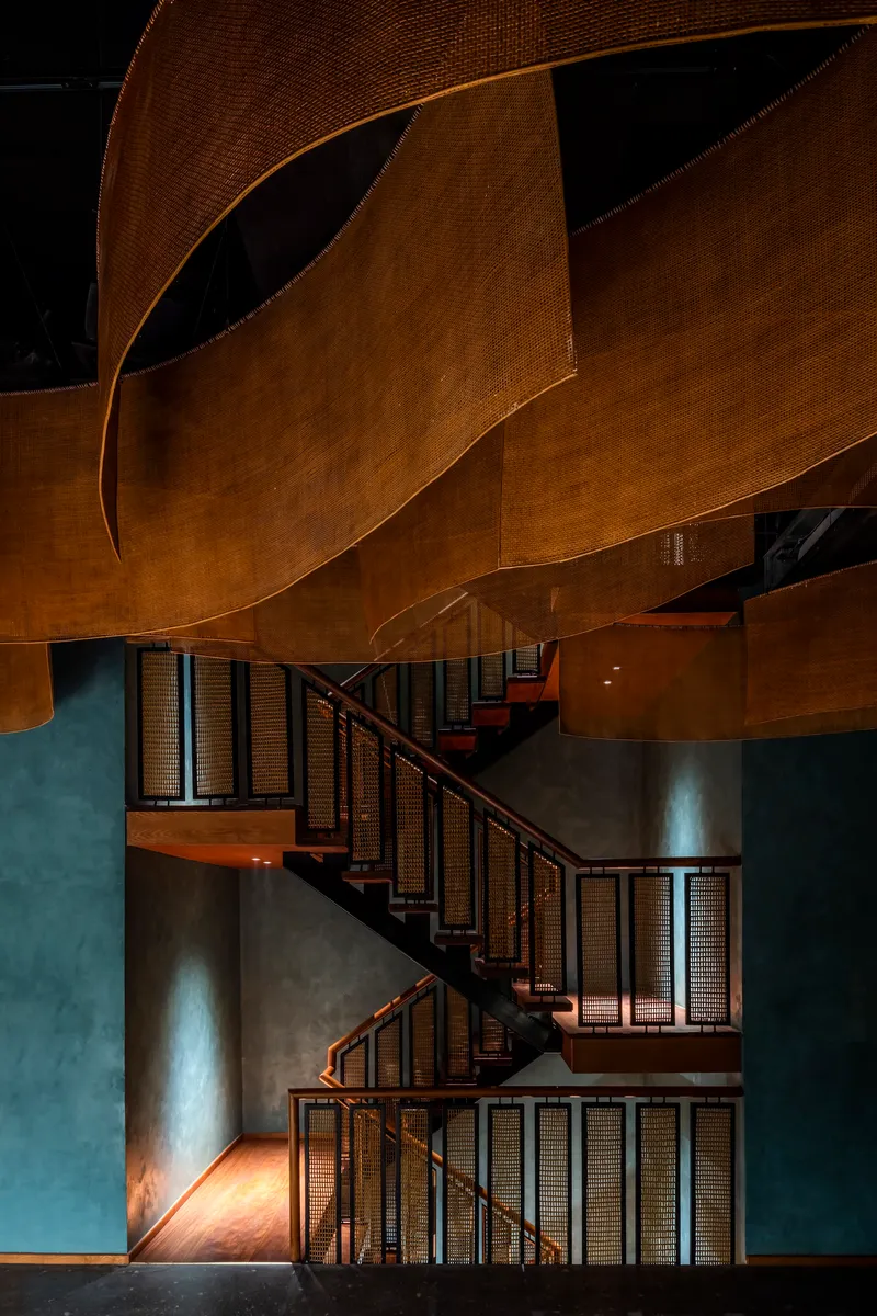 Switchback staircase with woven panel balustrades beneath curving woven ceiling forms under ambient lighting