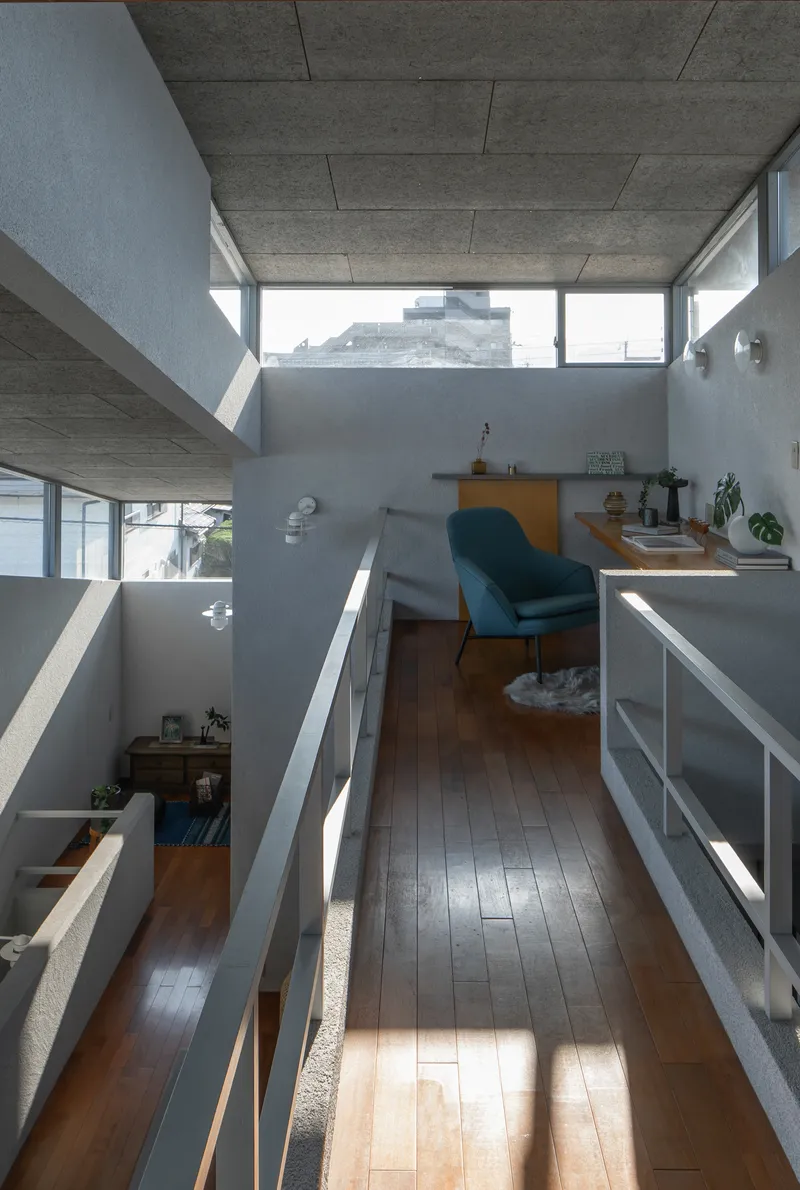 Upper-level hallway overlooking split-level interior spaces with exposed concrete ceiling and angular clerestory windows
