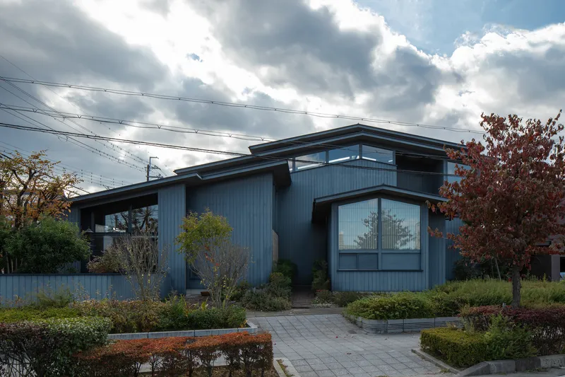 Entrance facade with vertical metal siding and planted pathway under dramatic cloudy sky