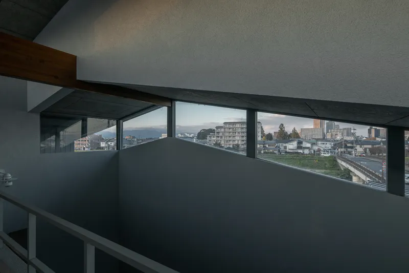 Upper-level interior corridor with horizontal band windows framing distant mountains and residential neighborhood at dusk