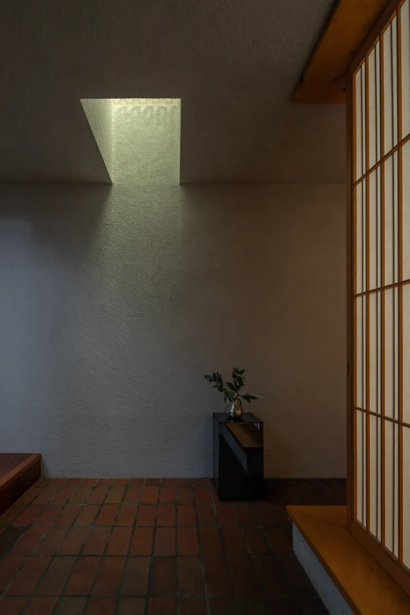 Entry hall with trapezoidal skylight casting geometric shadows on textured plaster wall beside wooden screen door