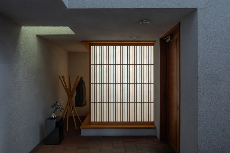 Foyer with floor-to-ceiling slatted wooden screen and square skylight above terracotta tile floor