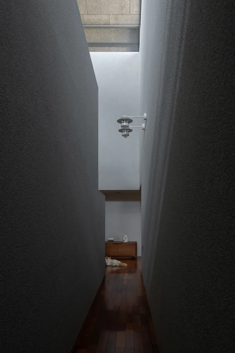 Narrow corridor with textured plaster walls opening to a skylit space beyond