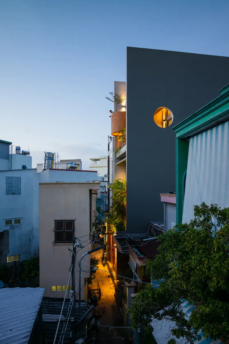 Narrow facade with circular porthole window rising above neighboring rooftops in the evening