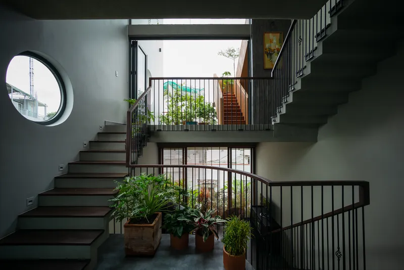 Multi-level staircase with circular window, metal balustrades, and potted plants on concrete landings in natural light