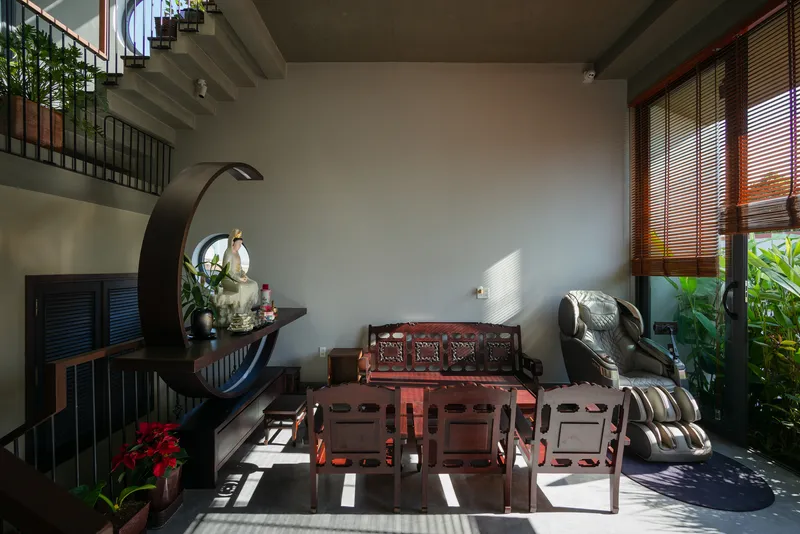 Double-height living room with carved timber furniture and horizontal wood blinds filtering afternoon sunlight