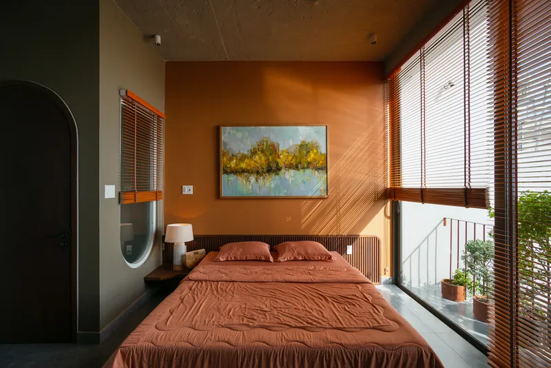 Bedroom with terracotta walls and horizontal wood blinds beneath an exposed concrete ceiling at dusk