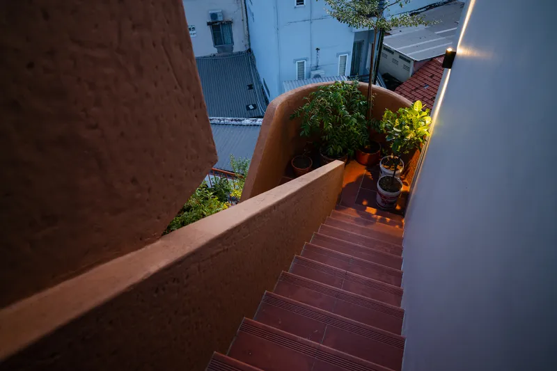 Rooftop stair with textured red tile treads descending between planted beds at evening
