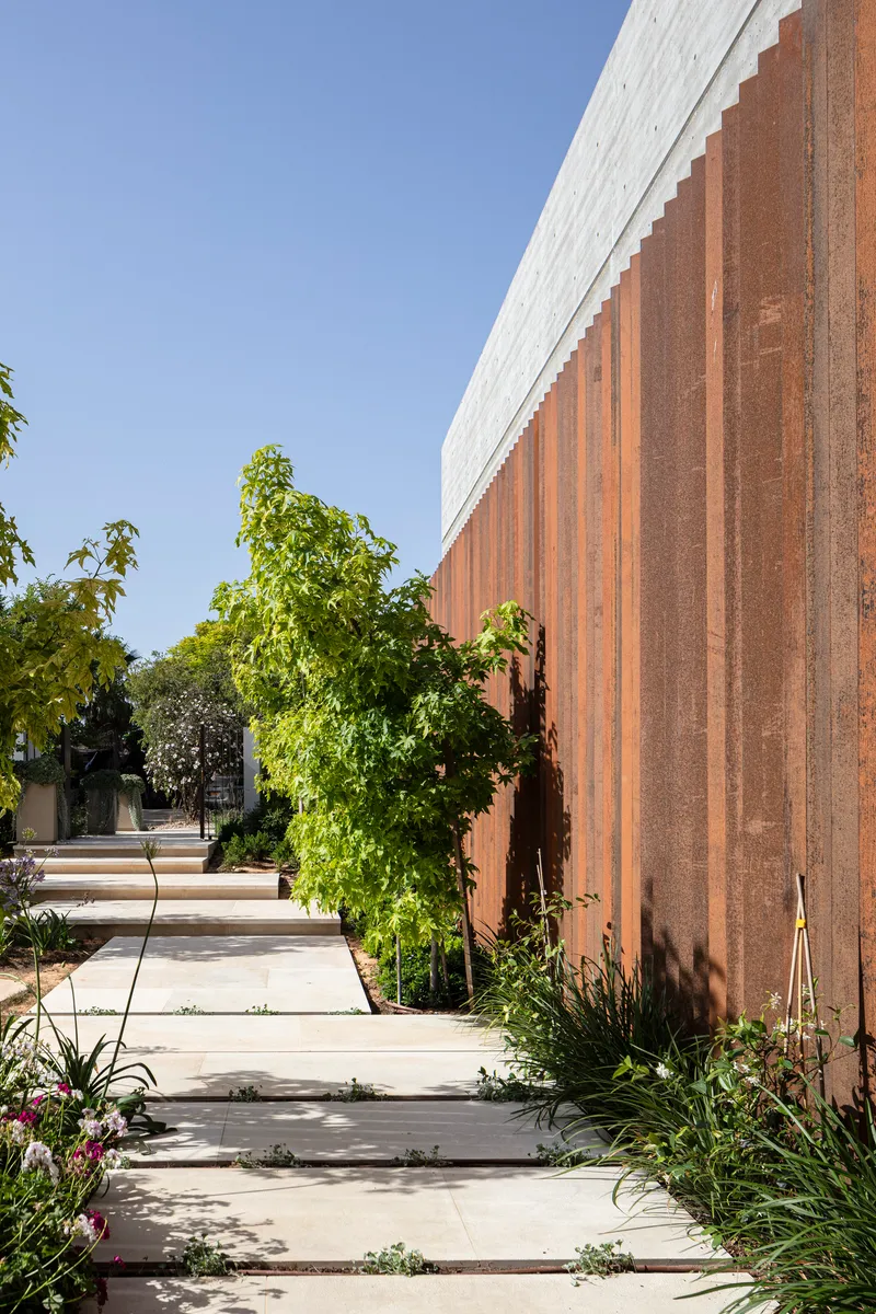 Weathered steel vertical cladding alongside a stepping stone path edged with planted beds